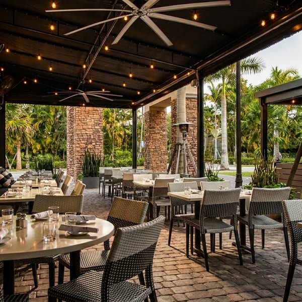 An inviting outdoor patio dining area with set tables, comfortable seating, and lush tropical foliage.