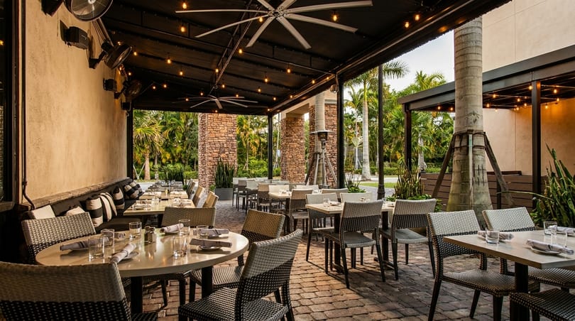 An inviting outdoor patio dining area with set tables, comfortable seating, and lush tropical foliage.