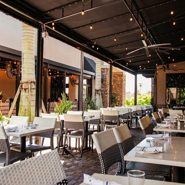 An inviting outdoor patio dining area with tables, chairs, string lights, and lush greenery.