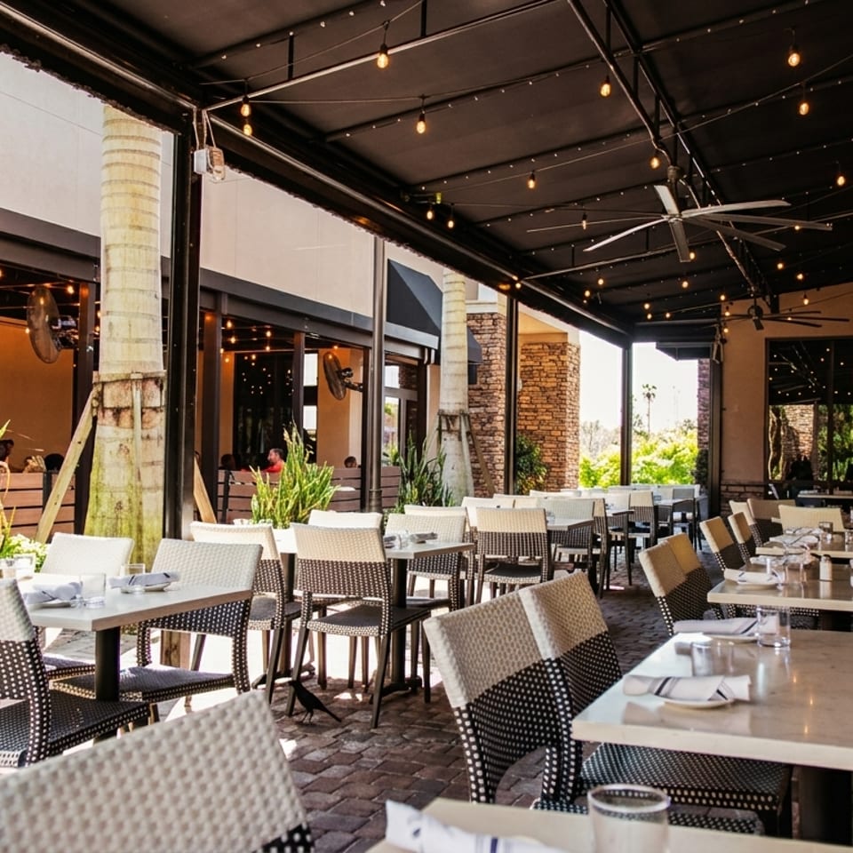 Spacious outdoor patio dining area with tables, chairs, string lights, and a long cushioned bench.