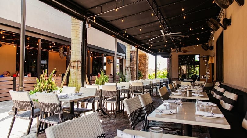 An inviting outdoor patio dining area with tables, chairs, string lights, and lush greenery.