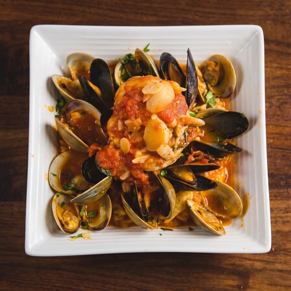Seafood pasta topped with mussels, clams, shrimp, garlic, and tomato sauce on a white square plate.