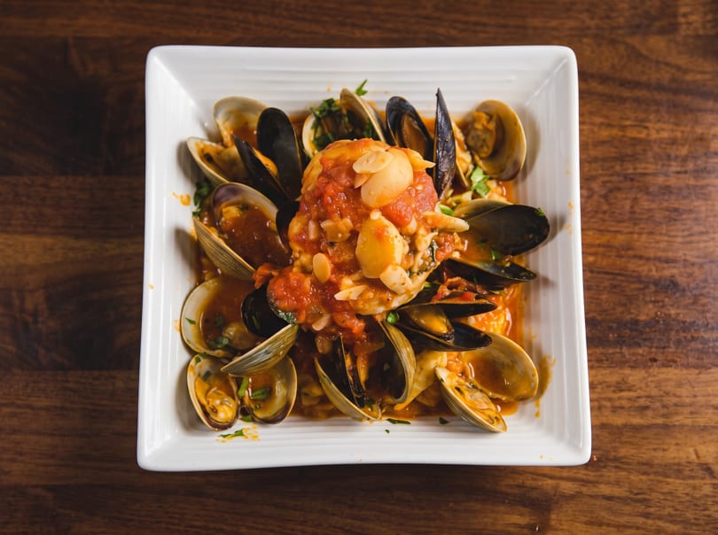 Mussels and clams in a savory red sauce with garlic, served in a white square dish.