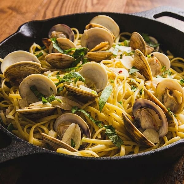 Linguine with clams, garlic, and fresh herbs in a black cast iron skillet on a wooden table.