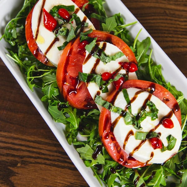 Caprese salad with sliced tomatoes, mozzarella, basil, red peppers, and balsamic glaze on arugula.