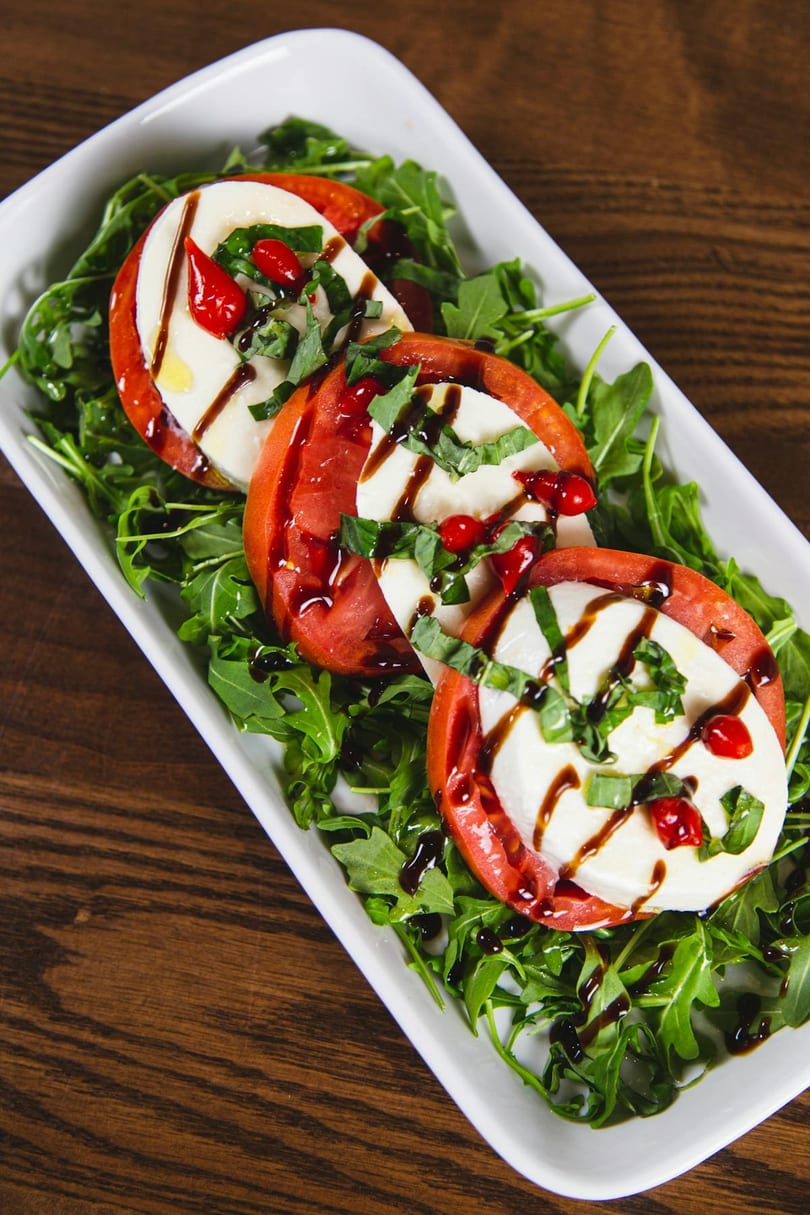 Caprese salad with sliced tomatoes, mozzarella, basil, red peppers, and balsamic glaze on arugula.