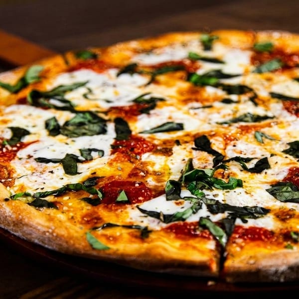 Freshly baked Margherita pizza with melted mozzarella, red sauce, and basil on a wooden table.