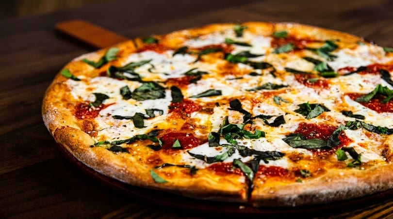 Freshly baked Margherita pizza with melted mozzarella, red sauce, and basil on a wooden table.
