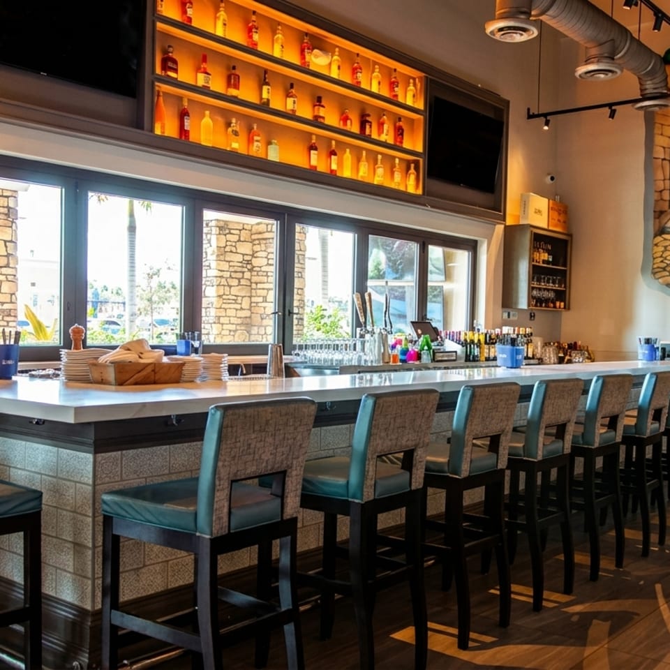 A long, well-lit bar with stools, a chalkboard menu, and a "Ciao Bella!" mural.