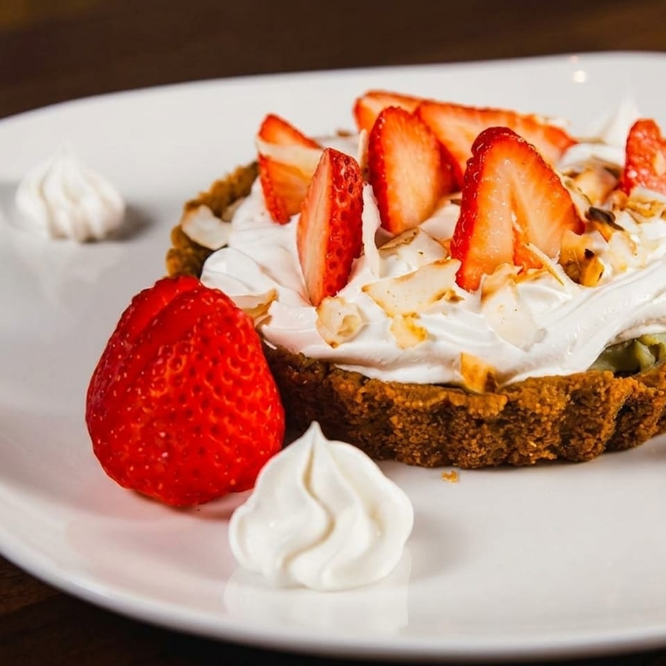 Strawberry tart with whipped cream, sliced strawberries, and meringue dollops on a white plate.