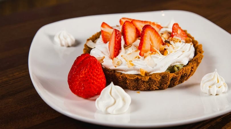 Strawberry tart with whipped cream, sliced strawberries, and meringue dollops on a white plate.
