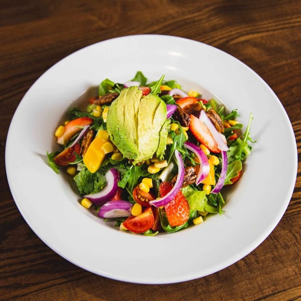 Colorful salad with avocado, strawberries, corn, red onion, and pecans in a white bowl.